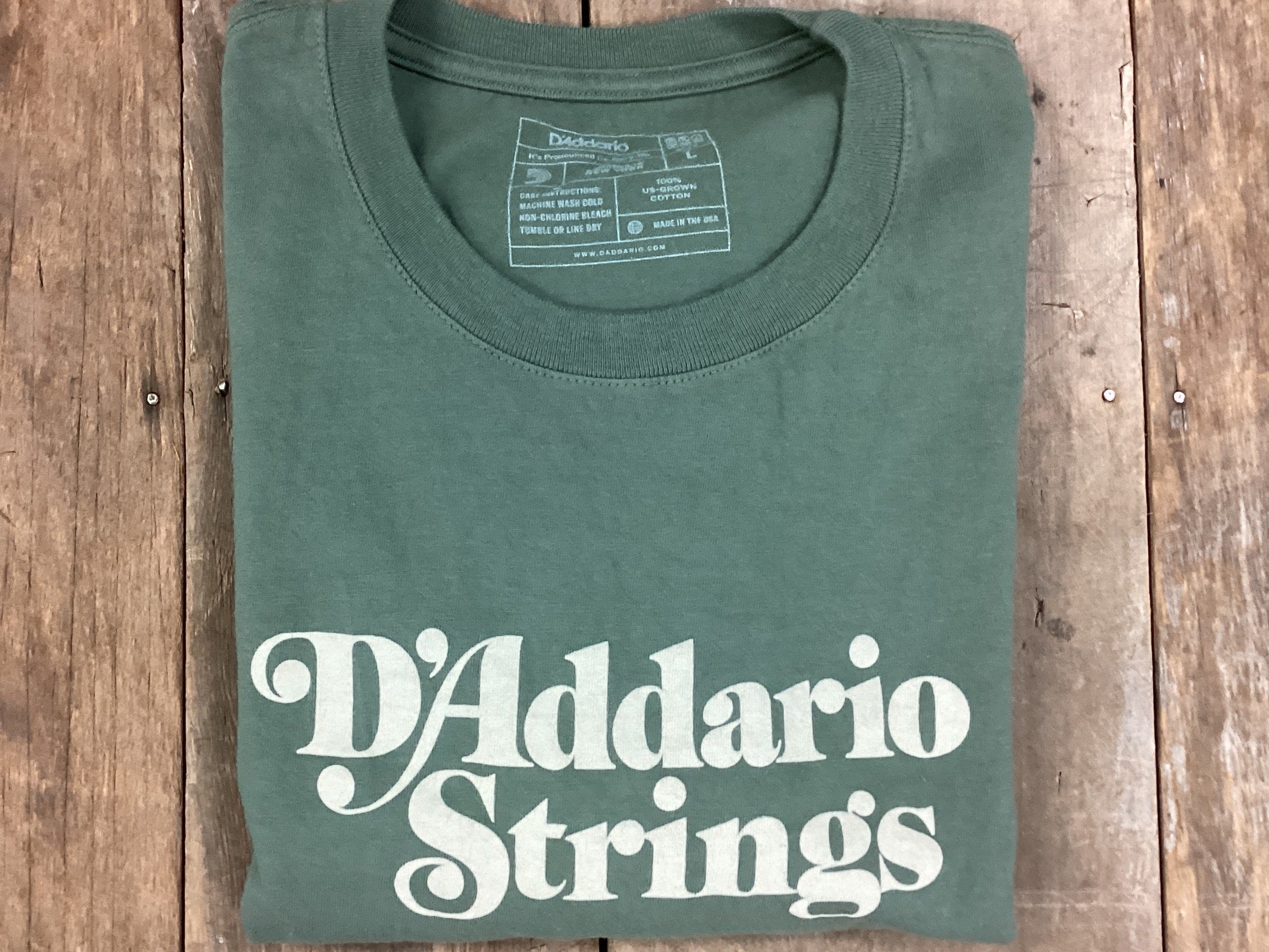 Folded green t-shirt with 'D'Addario Strings' text on a wooden surface