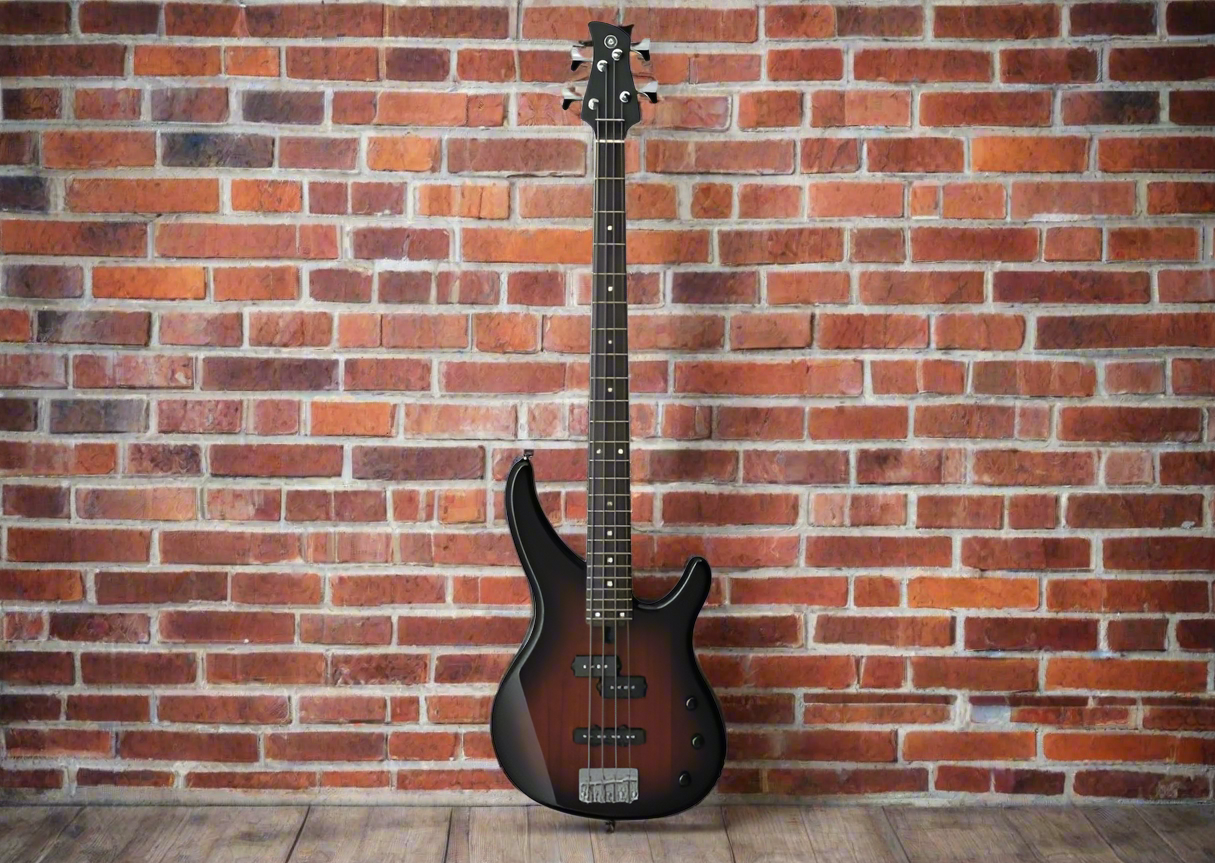 Image of A 4-string electric bass guitar with an old violin sunburst finish leaning against a brick wall.