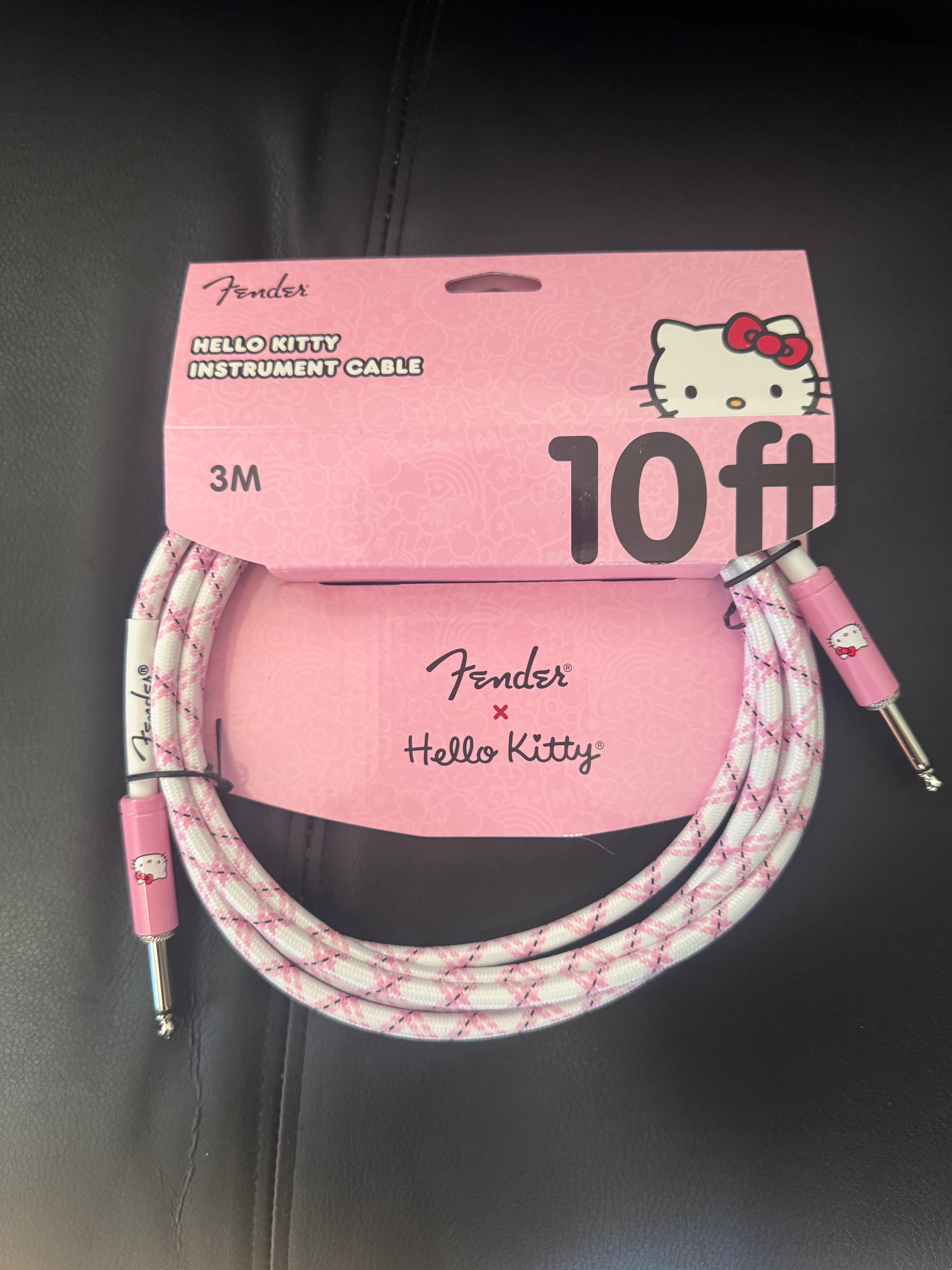 Image of Fender x Hello Kitty instrument cable with pink packaging on a dark background