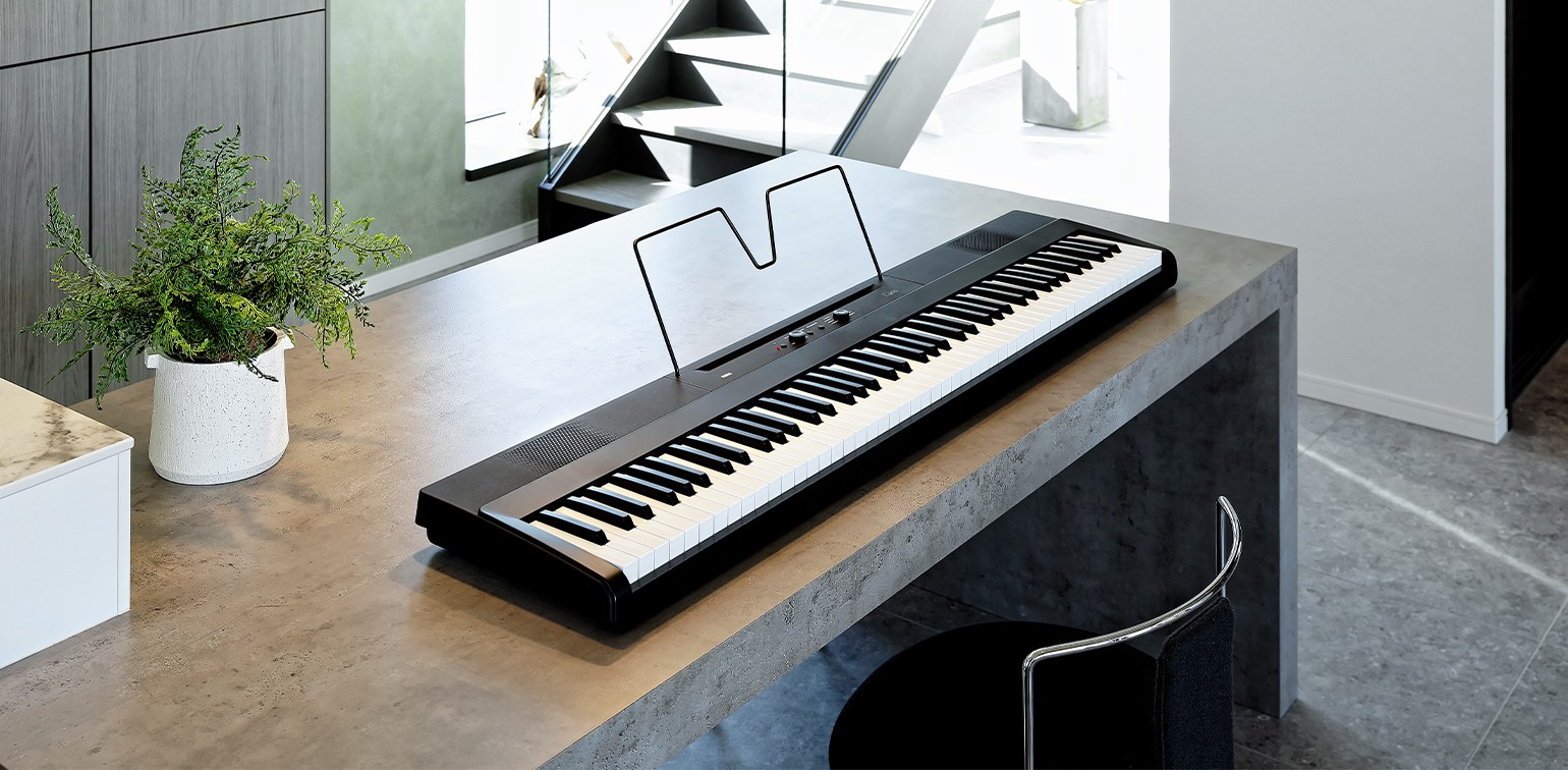 Image of A KORG Liano 88 Key Digital Piano placed on a countertop in a bright kitchen setting, showing the keyboard and sustain pedal.