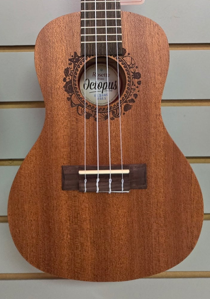 Image of A wooden ukulele with a warm brown finish, featuring a decorative floral inlay around the soundhole and a white brand label that reads 'Riken Octopus'.